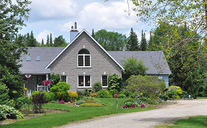 A modern, two-storey grey brick country home with gardens and a gravel driveway.